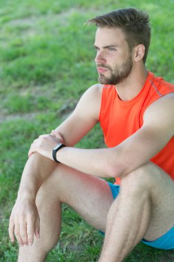 Spor araç konsepti. Atlet fitness izci veya adım sayar. Adam atlet sakin yüz rahatlatıcı, Doğa arka plan üzerinde. Sporcu pedometre gadget ile eğitim. Adam akıllı saat takan çimenlerin üzerinde oturur