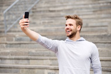 Sakallı bir adam akıllı telefonlu, merdivenli şehir geçmişi olan bir adam. Adam blogcu akıllı telefondan video konferansı yapıyor. Blogger konsepti. Blogcu videoyu çevrimiçi yayınlamak için akıllı telefon kullanır