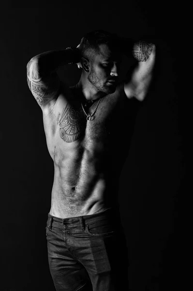 Fisiculturista com bíceps e tríceps. Homem tatuado mostra torso muscular sexy. Esportista com seis maços e abdominais. Modelo de moda com tatuagem em jeans. Cuidado com o corpo com fitness e esporte, preto e branco — Fotografia de Stock