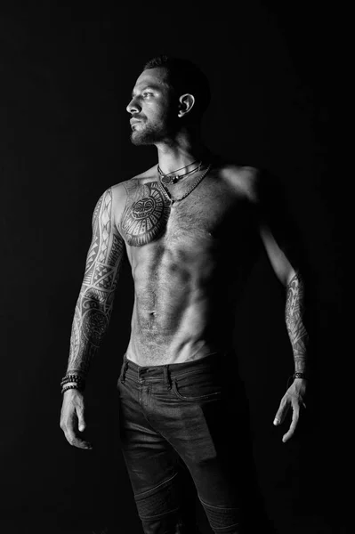 El hombre tatuado muestra un sexy torso muscular. Deportista con seis paquetes y ab. Culturista con bíceps y tríceps. Modelo de moda con tatuaje en jeans. Cuidado del cuerpo con fitness y deporte, blanco y negro — Foto de Stock