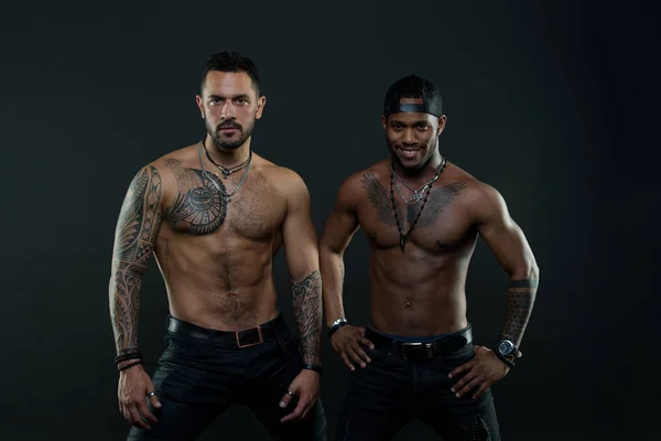 Machos with muscular tattooed torsos look attractive, dark background. Athletes on confident faces with nude muscular chests. Guys sportsmen with sexy muscular torsos. Masculinity concept