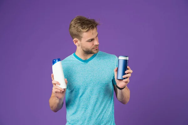 Macho mantenga botellas de champú y gel sobre fondo violeta. Hombre de camiseta azul con tubos sobre fondo púrpura. Cuidado de la piel y el cabello. Salud y salud. Cosmético para spa y bañera o ducha . — Foto de Stock