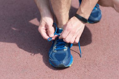 Ayakkabı bağcıklarını bağlayan eller, arka plan çalışması. Spor ayakkabı bağcığını spor ayakkabısına bağlayan bir sporcunun elleri. Koşu ekipmanı konsepti. Erkek eli ile bağlayan ayakkabı bağcıkları