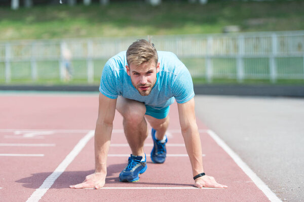 Man runner on start position at stadium. Runner in start pose on running surface. Man run outdoor at running track. Sport and athletics concept. Sportsman on concentrated face ready to go