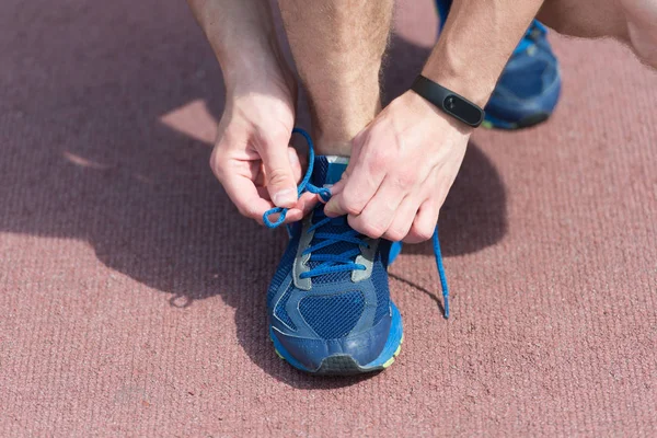 Hands tying shoelaces on sneaker, running surface background. Hands of sportsman with pedometer tying shoelaces on sporty sneaker. Running equipment concept. Shoelaces tying by male hands — Stock Photo, Image