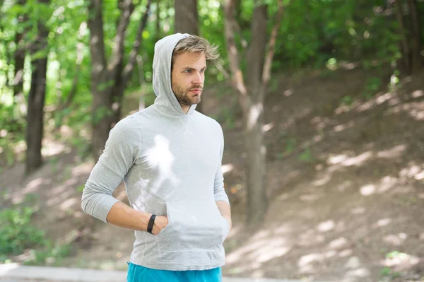 Тренування спортсмена з педометром. Спортсмен з щетиною з фітнес-трекером або педометром. Концепція спортивного гаджета. Спортсмен на суворому обличчі позує зі спортивним обладнанням, фоном природи — стокове фото