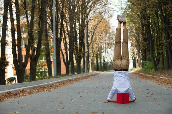 Man stand on head on park road. Student with book upside down in autumn outdoor. Work life balance. Education and knowledge. Yoga exercise headstand and sport