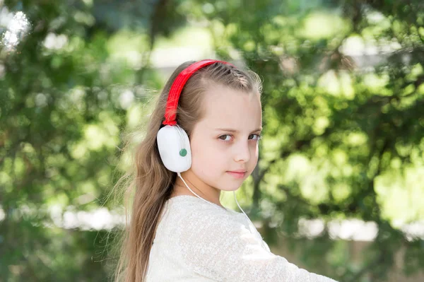 子供は、屋外のヘッドフォンで音楽をお楽しみください。小さな女の子は、夏の公園で音楽を聴きます。ファッションの子供と現代のテクノロジー。メロディーの音と mp3。夏休み楽しく — ストック写真