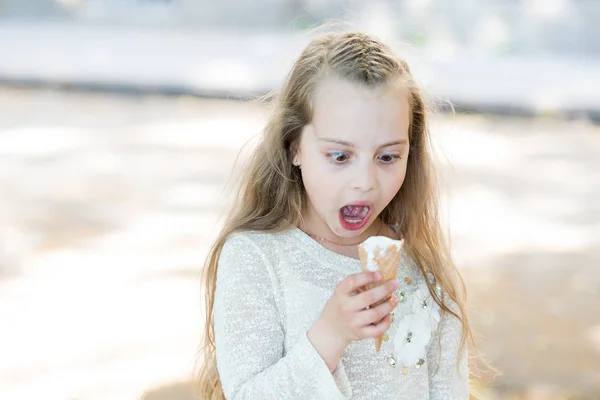 Ragazzina con cono gelato in mano. Estate tratta concetto. Bambina golosa con gelato bianco in cono di cialda. Ragazza golosa su viso scioccato mangia gelato, sfondo chiaro — Foto Stock