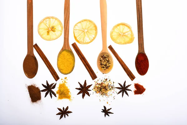 Composition of spoons with spices and dried oranges. Culinary art concept. Spoons filled with kitchen herbs and spices. Spoons with spices as red pepper, curcuma and cinnamon on white background