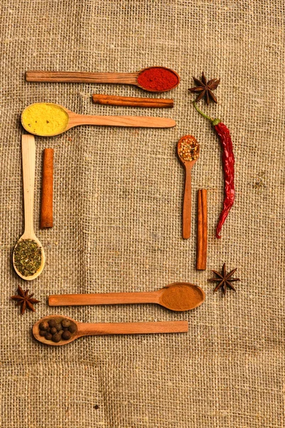 Spoons with spices as red pepper, curcuma and cinnamon on sackcloth background. Composition made out of spoons with spices. Spoons filled with kitchen herbs and spices. Condiments and spices concept