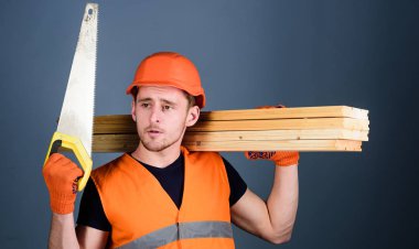 Dostum, kask, kask içinde tamirci el testeresi, keskin bıçak, gri arka plan bakar tutar. Marangoz kavramı. Marangoz, woodworker, işçi, düşünceli yüz taşıdığı ahşap kirişler omuz üzerinde Oluşturucu