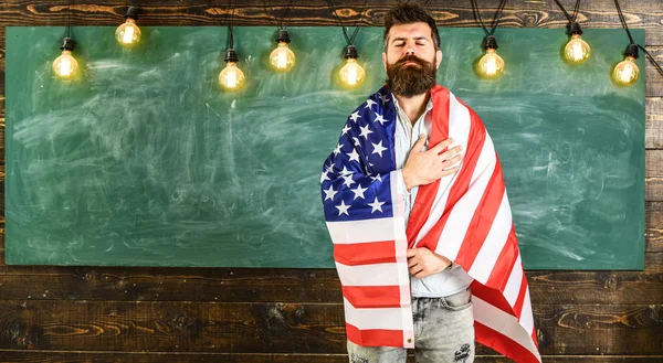 Conceito de educação patriótica. Professor ensina a amar a pátria, EUA. Homem com barba e bigode no rosto sério com bandeira dos EUA, quadro-negro no fundo. Professor americano coberto com bandeira americana — Fotografia de Stock