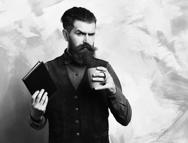 Γενειοφόρος κτηνώδης καυκάσιος hipster με φλιτζάνι καφέ και μαύρο σημειωματάριο — Φωτογραφία Αρχείου