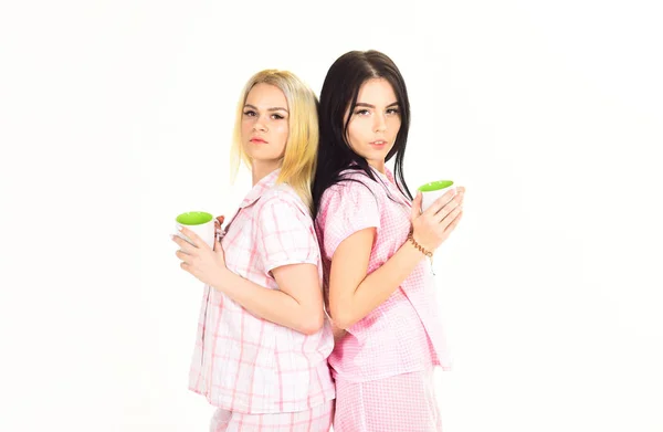 Meninas bebendo café de manhã, fundo branco isolado. Conceito de café da manhã. Loira e morena em rostos sonolentos segura canecas com café. Irmãs ou melhores amigos de pijama ficar de volta para trás — Fotografia de Stock