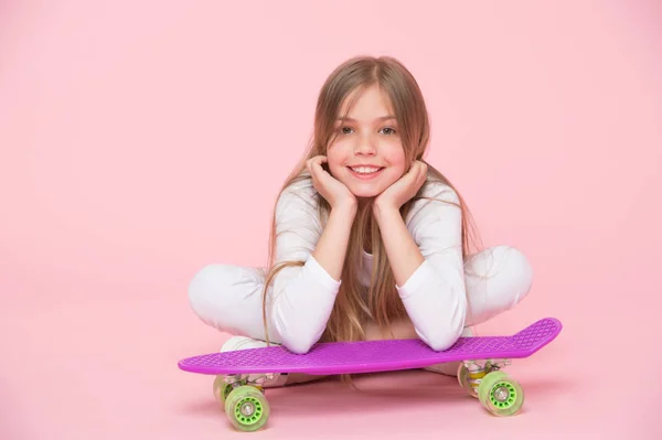 Miúdo de skate deitado no chão sobre fundo rosa. Criança patinadora sorrindo com longboard. Menina pequena sorriso com skate bordo. Estilo de vida infantil e jogos ativos. Atividades esportivas e energia, pastel punchy — Fotografia de Stock