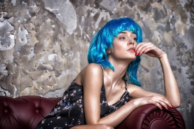 Mavi peruk, beton duvar arka plan poz düşünceli yüzündeki ne? Mavi saçlı kadın sıradışı ve olağanüstü görünüyor. Ucube kavramı. Bayan ucube sıradışı görünümü ile