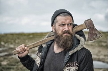 Sakallı adam paslı balta doğal arka plan üzerinde tutun. Şapkasını ve ceket açık hippi. Sakal ve bıyık üzerinde ciddi bir yüz olan adam. Keşif ve macera. Kamp ve yolculuk tutkusu, vintage filtre