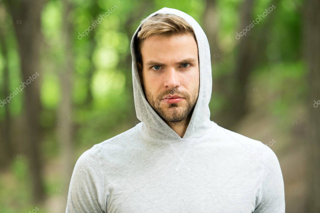 Guy bearded and attractive cares about his appearance. Man with bristle on serious face, nature background, defocused. Skin care concept. Man with beard or unshaven guy looks handsome hooded