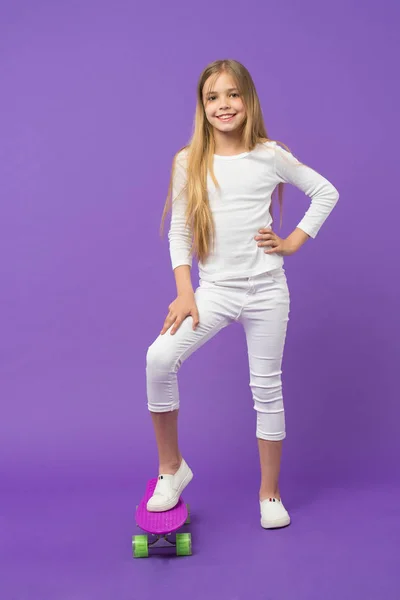 紫色の背景にカジュアルな服装でスケートの子供。女の子スケーターのロングボードを浮かべてします。スケート ボードと小さな子供の笑顔。スポーツ活動とエネルギー。小児期のライフ スタイルとアクティブなゲーム — ストック写真