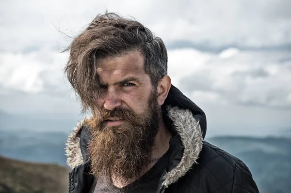 Man with brutal bearded appearance, brutal unshaven man looks untidy. Man with long beard and mustache wears jacket. Hipster on strict face with beard looks brutally while hiking. Hermit concept — Stock Photo, Image