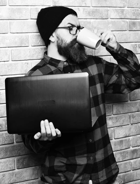 Barbudo brutal caucasiano hipster segurando laptop com copo — Fotografia de Stock