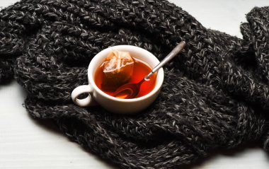 Kupa su, çay poşeti ve kaşık örme eşarp arka plan üzerinde kaynar ile dolu. Çay bardağı, çay de daldırma örme eşarp ile sarılmış. Sonbahar içki kavramı. İşlem bardağa demleme çay