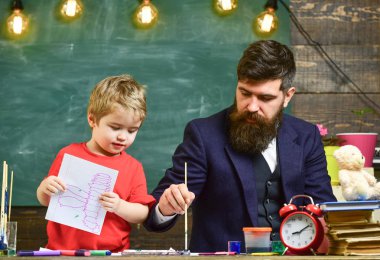 Baba oğluna suluboya nasıl kullanılır gösteriyor. Elinde çizim tutan sevimli bir çocuk. Yaratıcılık kavramı
