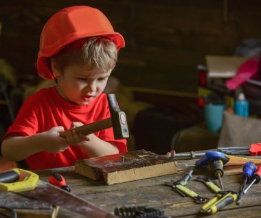Kask Oluşturucu veya repairer, onarımı veya handcrafting olarak oynayan sevimli çocuk. Meşgul yüz oyunlarında evde atölye üzerinde yürümeye başlayan çocuk. Kavram handcrafting. Çocuk Çocuk ahşap Pano çivi çekiç