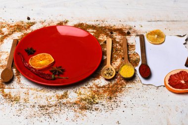 Baharat tüm ahşap yüzey üzerinde dağınık. Baharat öğütülmüş kırmızı biber ve curcuma toz olarak dağılmış. Mutfak konsepti. Tabak ve kaşık Beyaz ahşap zemin üzerinde kurutulmuş portakal ve serin biber ile