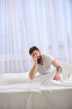 Akşamdan kalma kavramı. Adam sabah uyanma hayal kırıklığına acı yüzü. Sakal ve bıyık maço akşamdan kalma uğrar. Tişörtlü adam yatak uyanık, beyaz perde arka plan üzerinde oturur