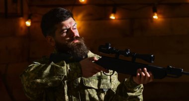 Sakallı adam ahşap iç arka planda kamuflaj elbiseler giyer. Maço gamekeepers evinde sıkı yüzünde. Avcı, av için hazır elinde tabanca ile acımasız hipster. Hakem kavramı