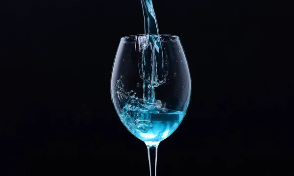 Enchimento de vinho com água com salpicos no fundo preto. Conceito de bebida refrescante. Cocktail com líquido azul em vidro. Vidro com água azul derramando com líquido com salpicos e gotas — Fotografia de Stock