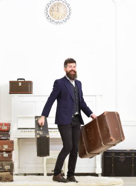Maço çekici, güler yüz üzerinde zarif vintage bavul taşır. Sakal ve bıyık Klasik takım elbise sunar Bagaj, lüks beyaz iç arka plan giyen adam. Butler ve hizmet kavramı