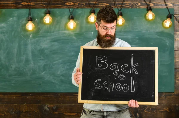 Πίσω στο σχολείο έννοια. Άνδρας με μούσι και μουστάκι για έκπληξη πρόσωπο καλωσορίζει φοιτητές, chalkboard σε φόντο. Δάσκαλος σε γυαλιά συγκρατεί Μαυροπίνακας με την επιγραφή στο σχολείο — Φωτογραφία Αρχείου