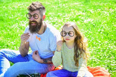 Zekice ve zekice bir fikir. Baba ve kızı yeşil arka planda çimlerin üzerinde oturuyorlar. Gözlüklerle poz veren çocuk ve baba çayırda fotoğraf kabini özellikleri. Aile dışarıda vakit geçirir.
