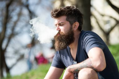 Gevşeme kavramı. Uzun sakallı ve bulutlar duman görünüyor rahat olan adam. Sakallı adam vape güneşli günde sigara içiyor. Adam sakal ve bıyık sakin yüzündeki defocused arka plan, dallarda