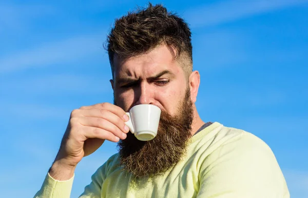 Homem barbudo com caneca de café, bebe café. Conceito de café gourmet. Homem com barba longa desfrutar de café. Homem com barba e bigode no rosto rigoroso bebe café, fundo céu azul, desfocado — Fotografia de Stock