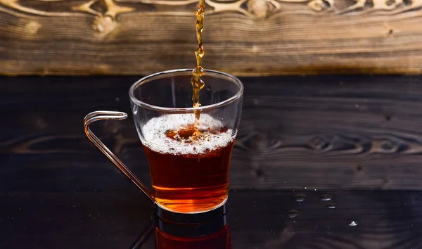 Glas mit Tee, das mit Flüssigkeit übergossen wird, mit Spritzern und Wassertropfen. Tee brauen Konzept. Becher mit Wasser oder Tee mit Spritzern auf dunklem Holzgrund — Stockfoto