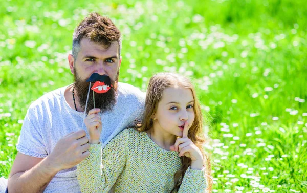 Aile açık havada eğlence harcamak. Çocuk sessizlik jest gösterirken booth öznitelik fotoğraf çocuk ve babası dudakları ile poz. Gizli kavramı. Baba ve kızı oturur, grassplot, arka planı yeşil çimenlerin üzerinde — Stok fotoğraf