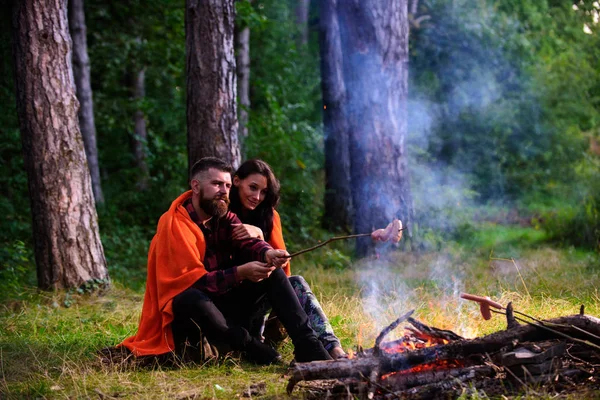 Young couple roast sausages on stick on bonfire in forest. — Stock Photo, Image