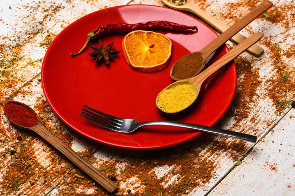 Concept culinaire. Épices comme le poivron rouge broyé et la poudre de curcuma dispersés. Assiette et fourchette avec orange séchée et poivre froid sur fond de bois blanc. Épices dispersées sur toute la surface en bois — Photo