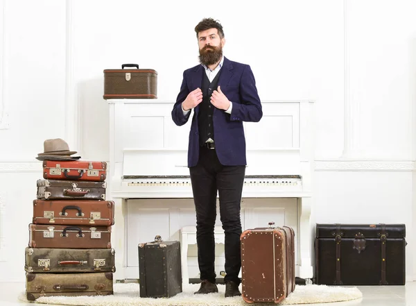 Hombre, viajero con barba y bigote con equipaje, lujoso fondo interior blanco. Macho elegante en la cara estricta se encuentra cerca de la pila de maleta vintage, listo para las vacaciones . — Foto de Stock