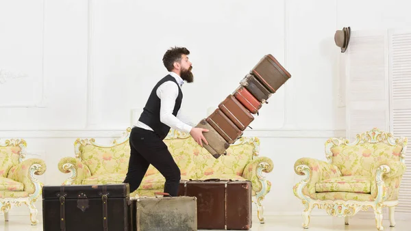 Gepäckversicherung. Mann mit Bart und Schnurrbart im klassischen Anzug liefert Gepäck, luxuriöses weißes Interieur. Portier, Butler stolperte versehentlich und ließ Stapel alter Koffer fallen — Stockfoto