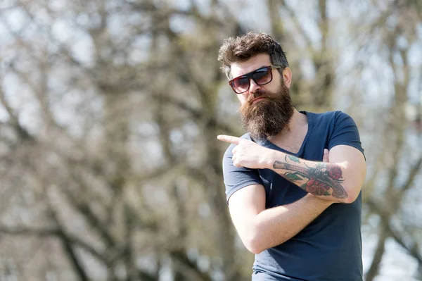 Hipster avec barbe semble élégant le jour ensoleillé. Homme avec barbe et moustache sur le visage strict pointant, fond de nature, déconcentré. L'homme barbu porte des lunettes de soleil élégantes. Mode et concept de style — Photo