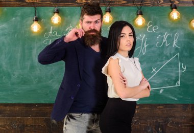 Adam sakallı ve seksi kız öğretmen stand sınıfta, kara tahta arka plan ile. Öğretmen ve sıkı öğretmen rahat görünüyor. Bayan ve birlikte okulda çalışan hippi. Ortaklar kavramı