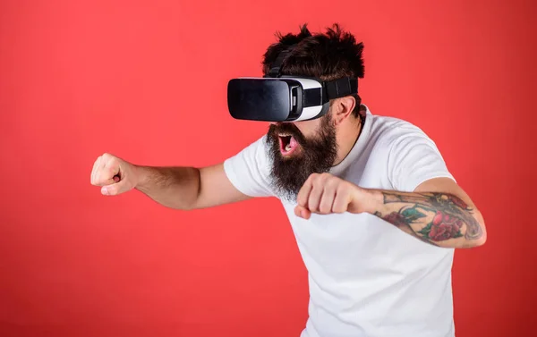 Hipster on excited face driving bike on high speed in virtual reality with modern digital gadget. Man with beard in VR glasses driving motorbike, red background. Virtual driving lessons concept — Stock Photo, Image