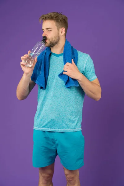 Homem bebe água depois de treinar em fundo violeta. Esportista sedento com garrafa de plástico no fundo roxo. Sede e desidratação. Água potável para a saúde. Actividade desportiva e energia — Fotografia de Stock