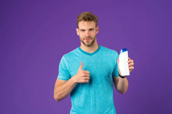 Hombre mostrar los pulgares hacia arriba con botella de champú sobre fondo violeta. Hombre barbudo como tubo de gel sobre fondo púrpura. Cuidado de la piel y el cabello. Salud y salud. Cosmético para spa y bañera o ducha —  Fotos de Stock