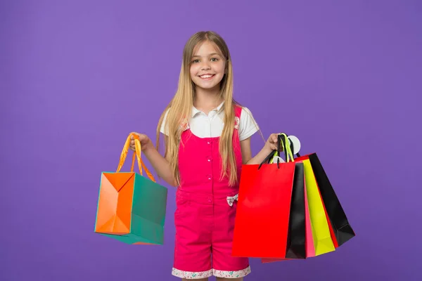 Flicka på leende ansikte bär klasar av påsar, isolerad på vit bakgrund. Tjejen gillar att köpa moderiktiga kläder i köpcentrum. Kid flicka med långt hår förtjust i shopping. Shopping koncept — Stockfoto